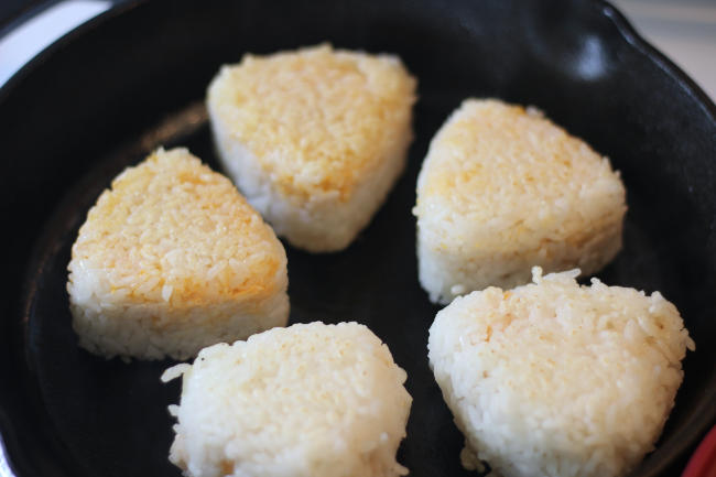 Photo of 5 golden brown onigiri in a cast iron skillet.