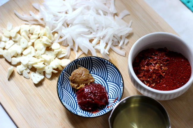 A display of sliced onion, sliced garlic, vegetable oil, chili flakes, and Korean soybean pastes.