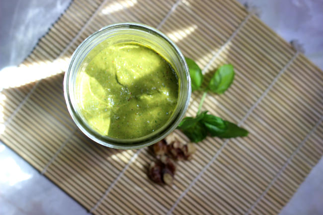 Walnut pesto in mason jar, with walnuts and basil leaves as decoration. Sunlight is shining on the pesto, making it glow and look more appetizing.