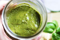 Picture of Walnut Pesto in a wide-mouth Mason Jar. Fresh, green basil leaves decorate the background.