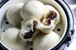 Picture of freshly steamed red bean buns sitting in a white steam basket.