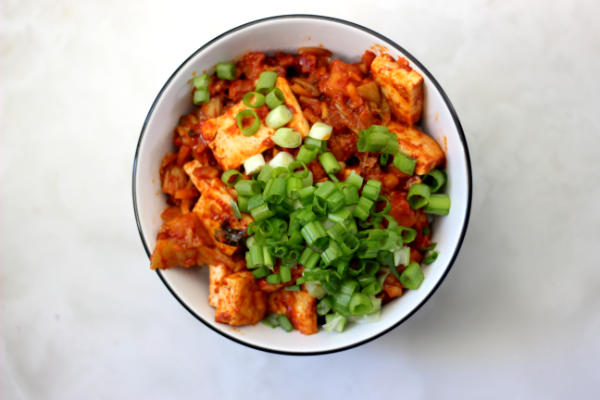 Bowl filled with kimchi tofu and topped with scallions.